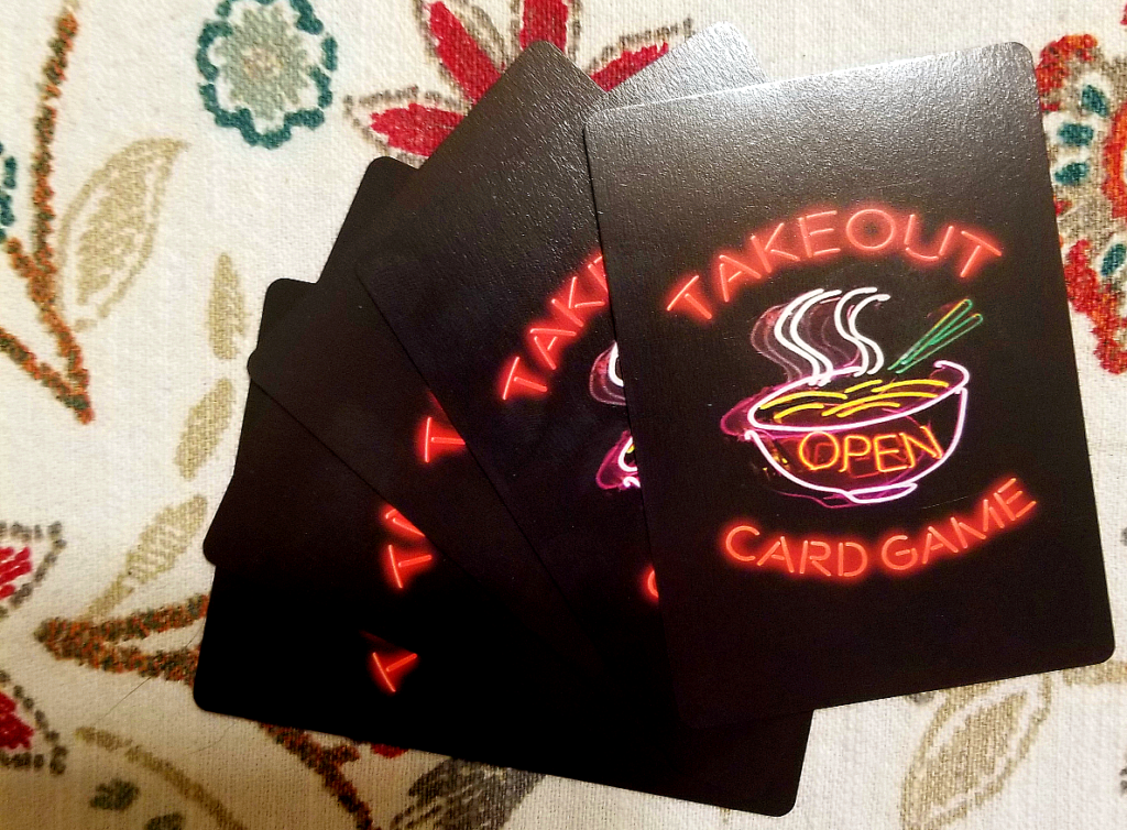 A fan of five cards, showing a black background and a design of a neon sign of a noddle bowl with chopsticks and "Takeout Card Game"