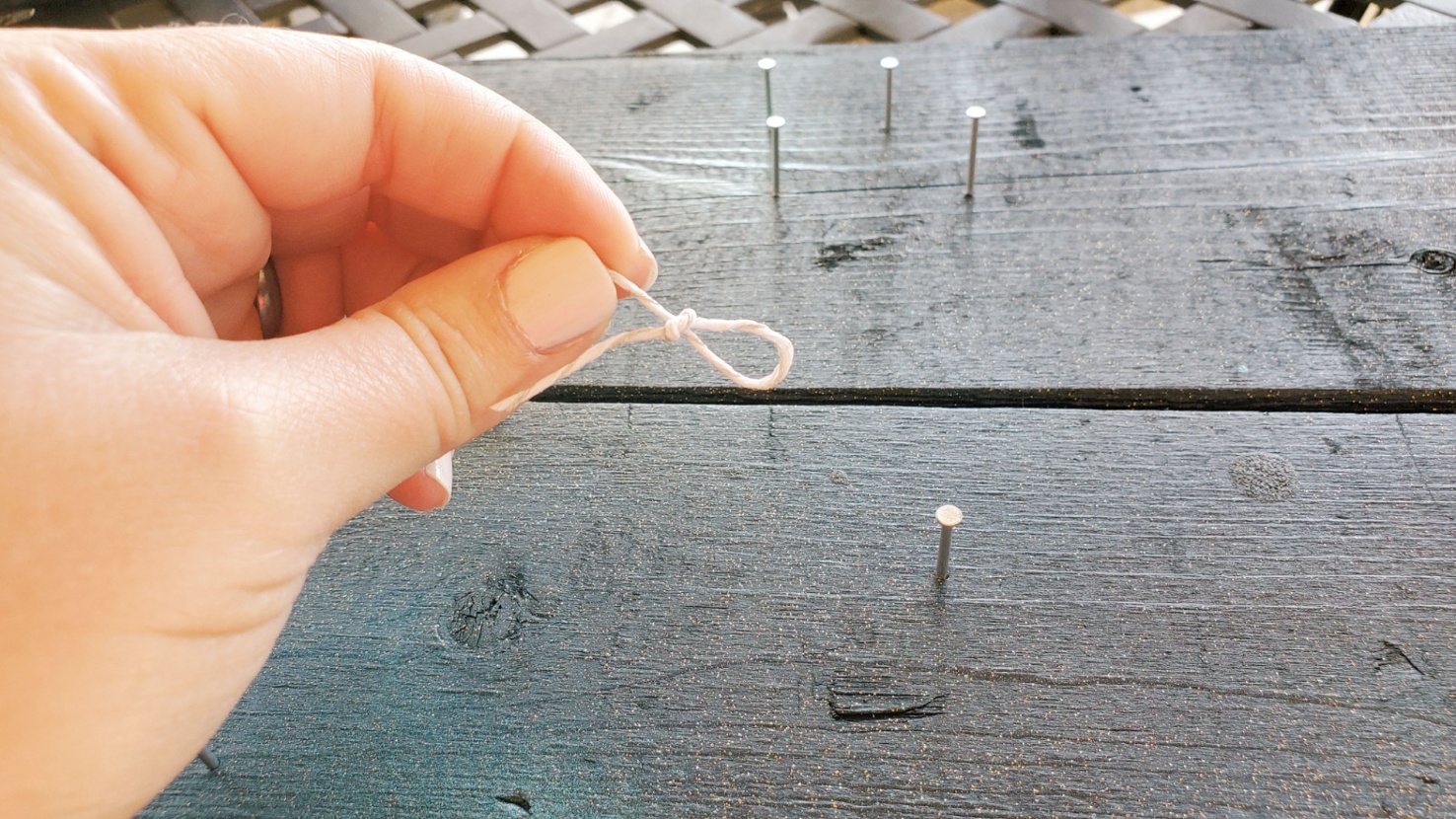 hand holds string with small slip knot over the wood piece with nails in it