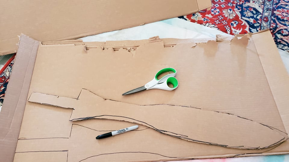 a sword shape traced out twice onto a large piece of cardboard and cut so that it makes mirrored pieces