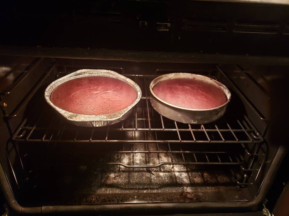 2 cake pans with reddish brown cake, baking in the oven