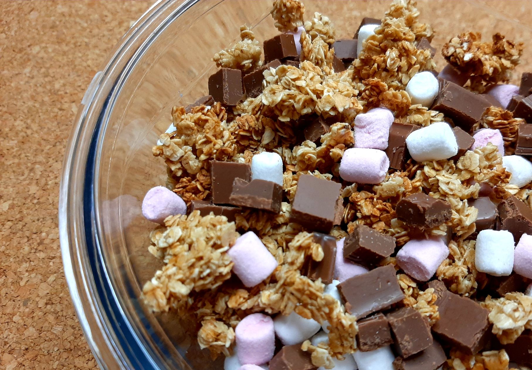 large granola pieces with chocolate chunks and mini marshmallows, in a glass bowl on a wooden surface