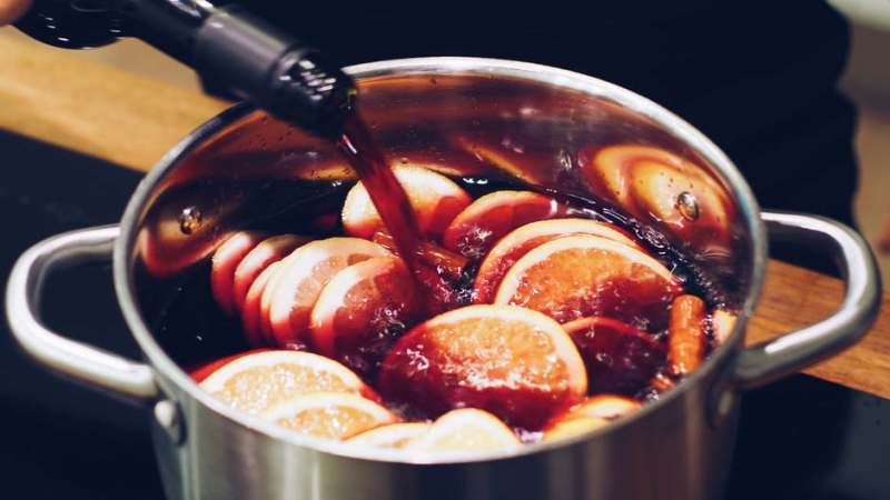 A large pot of glühwein, with red wine being poured over oranges and spices