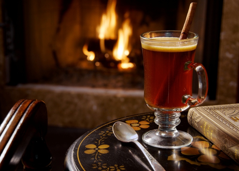 A glass mug of hot buttered rum placed before a fireplace.