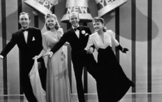 Screen capture of the cast from Holiday Inn (Bing Crosby, Marjorie Reynolds, Fred Astaire, and Virginia Dale) posed in front of a New Year's Eve stage background.
