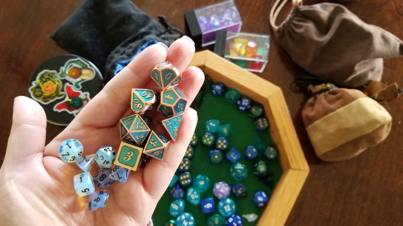 Joanna's polyhedral dice are a teal metallic with edge lines and numbers in gold.
