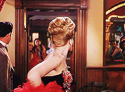 A moving GIF of a young Angela Lansbury; she is dressed as a saloon hostess with a red feather boa and turns to the camera, looking unimpressed.