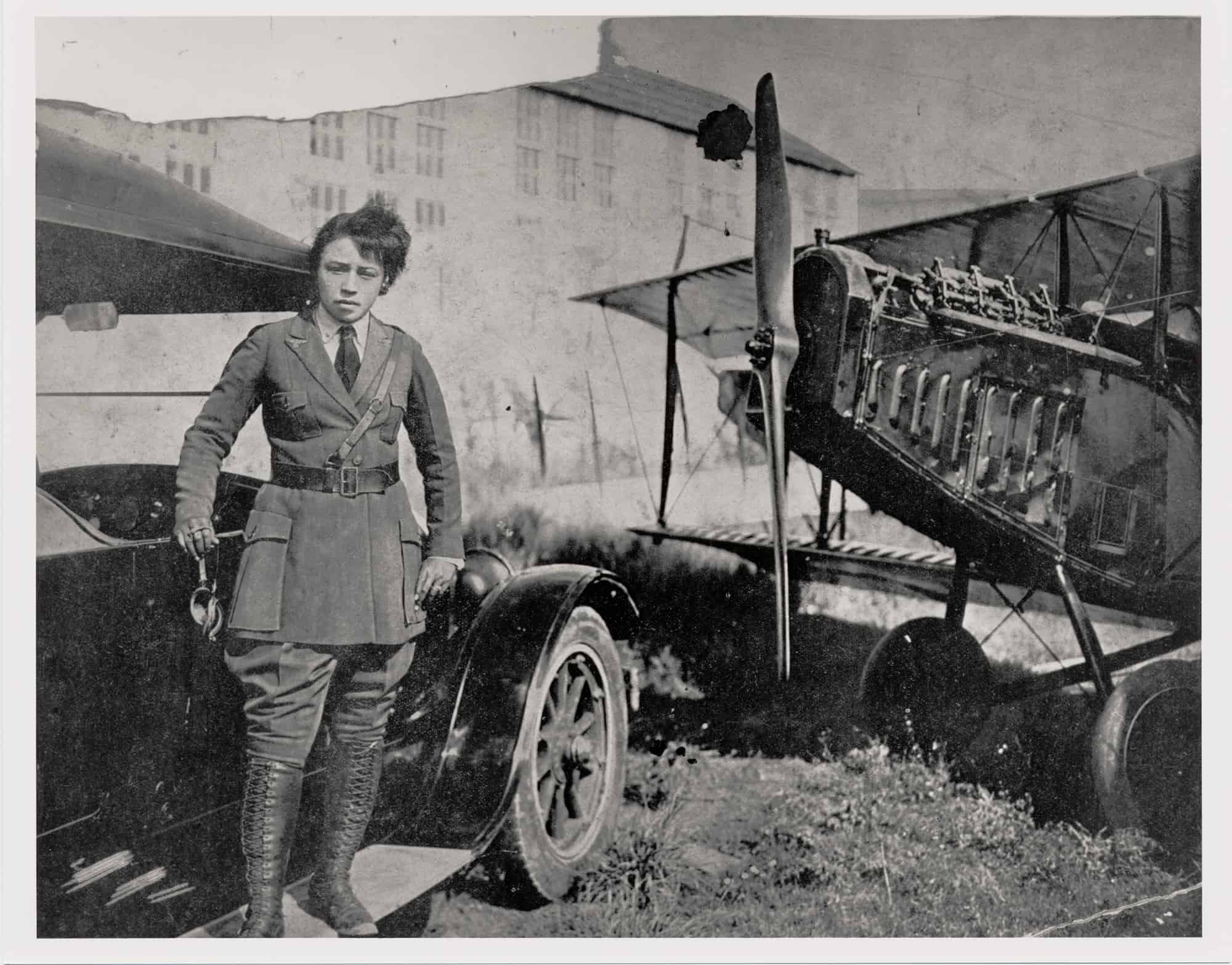 A black and white photo of the African American aviatrix, Bessie Coleman with her bi-plane