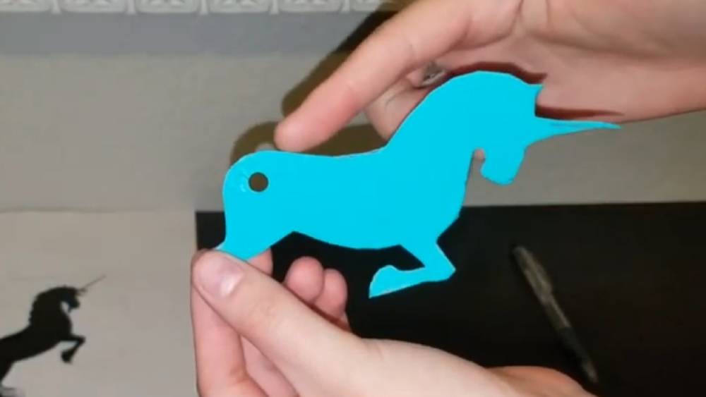 Cutout of unicorn figure on blue paper with a hole punched in the rear for attaching a tail