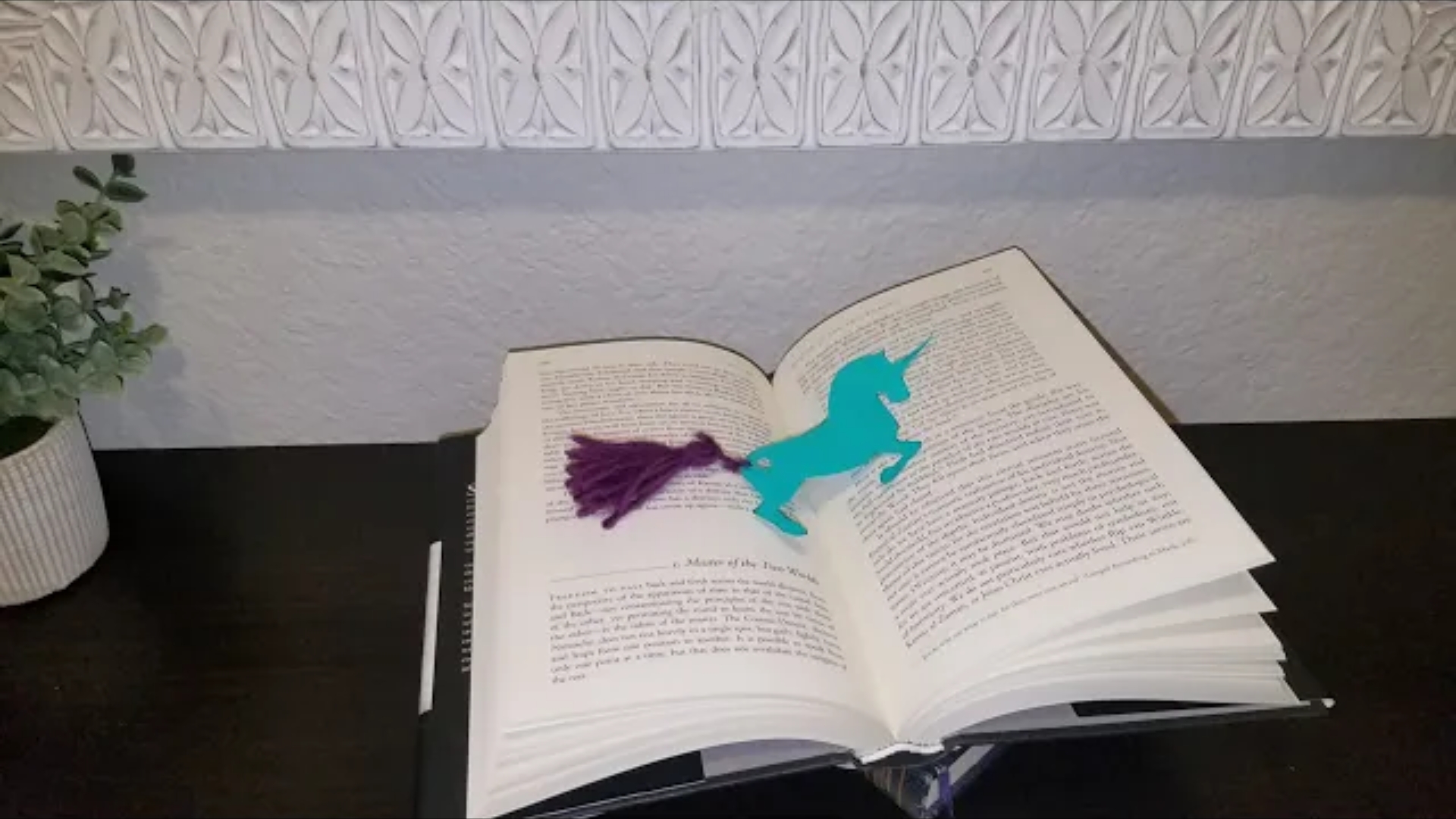 Blue unicorn bookmark with purple string tail sitting on an open book