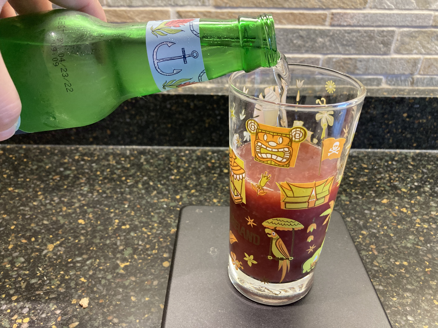 Pouring ginger ale into a glass that is half filled with mixed juices; mixed juices are a dark red color