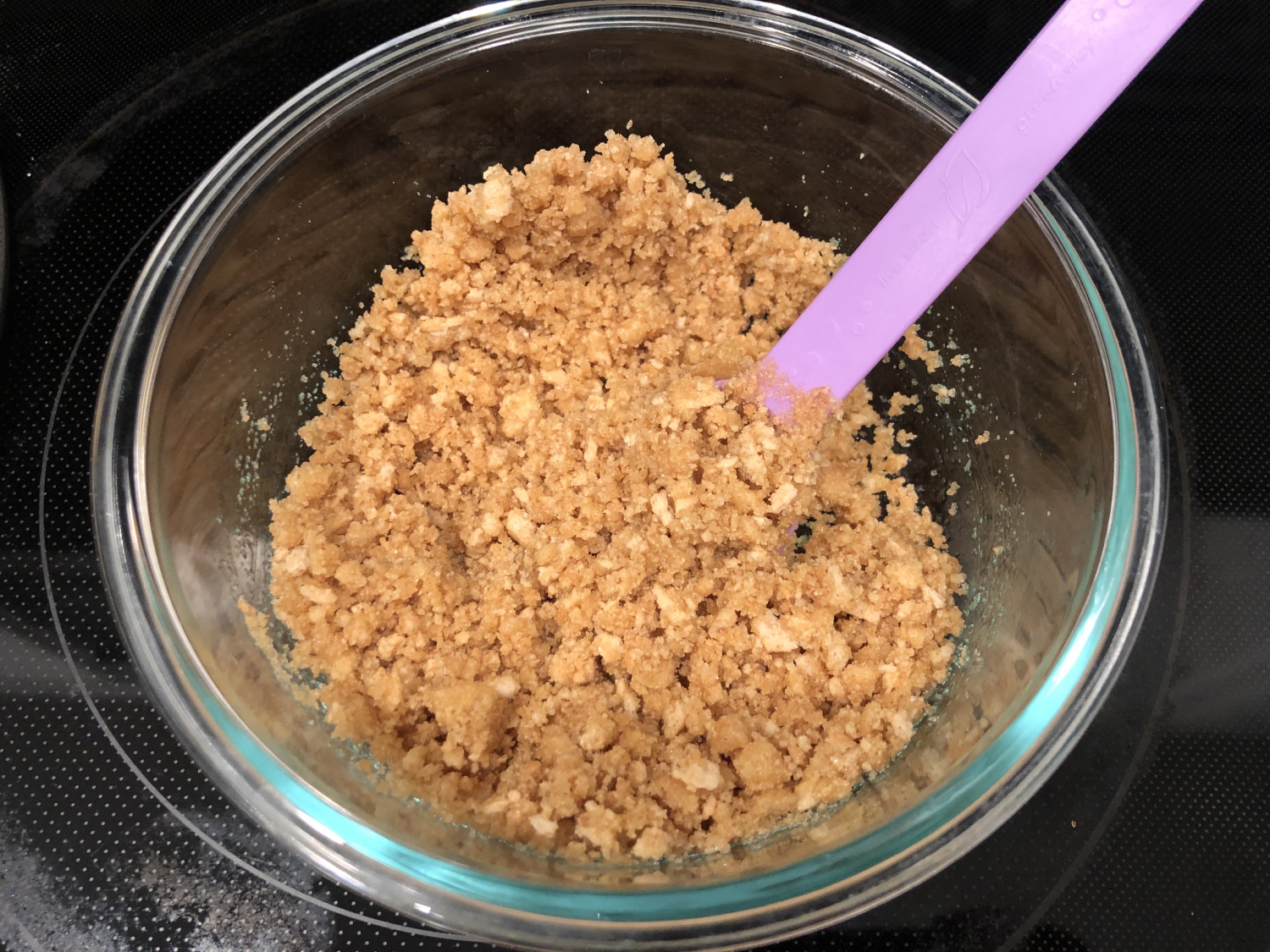 graham cracker and butter mixture in a bowl, with everything evenly combined using a purple spoon