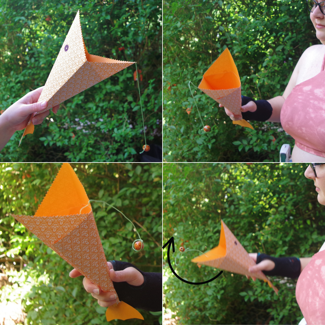 a person wearing a pink top plays with the fish and ball paper toy in front of a green leafy background