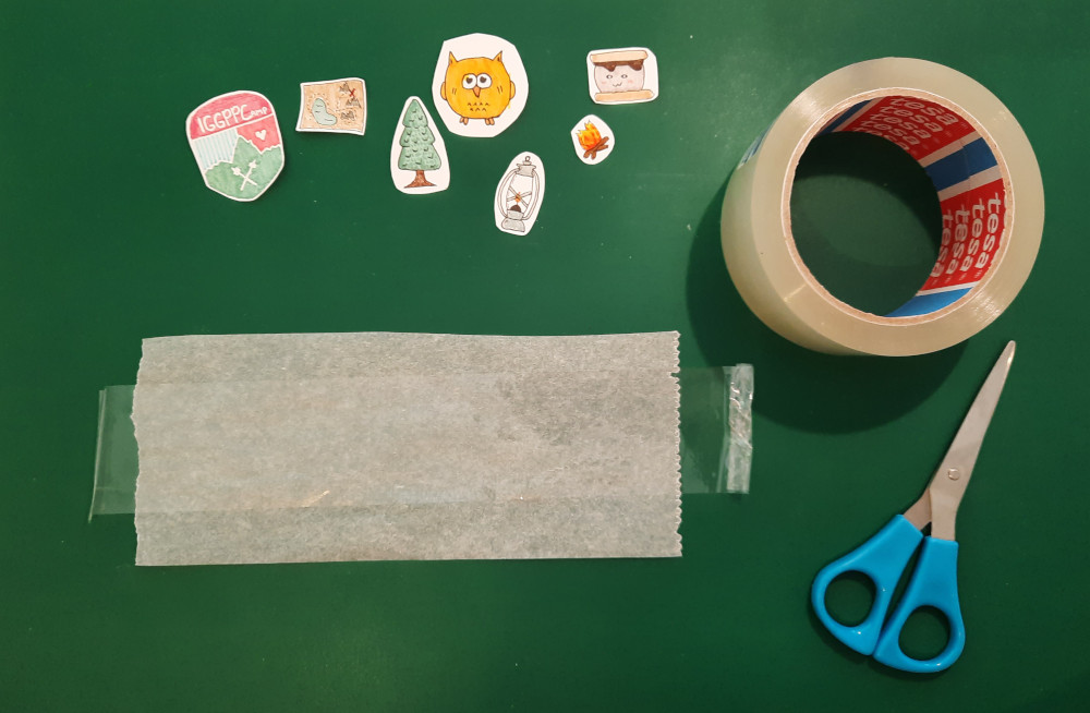 A bit of parchment paper is taped to a green surface. A pair of scissors and several cut out drawings are arrayed around it. 