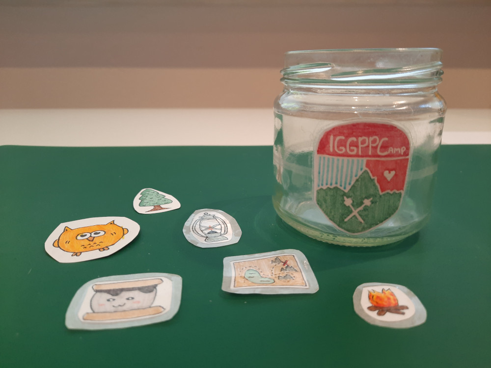 A homemade IGGPPCamp sticker is adhered to a small glass jar. Other homemade stickers are scattered around it.