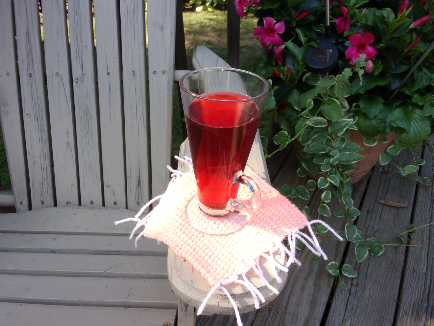 Enjoy your mug rug! This one is being enjoyed on a wooden patio with colorful flowers in the background, and a bright red drink in a glass is on the rug.