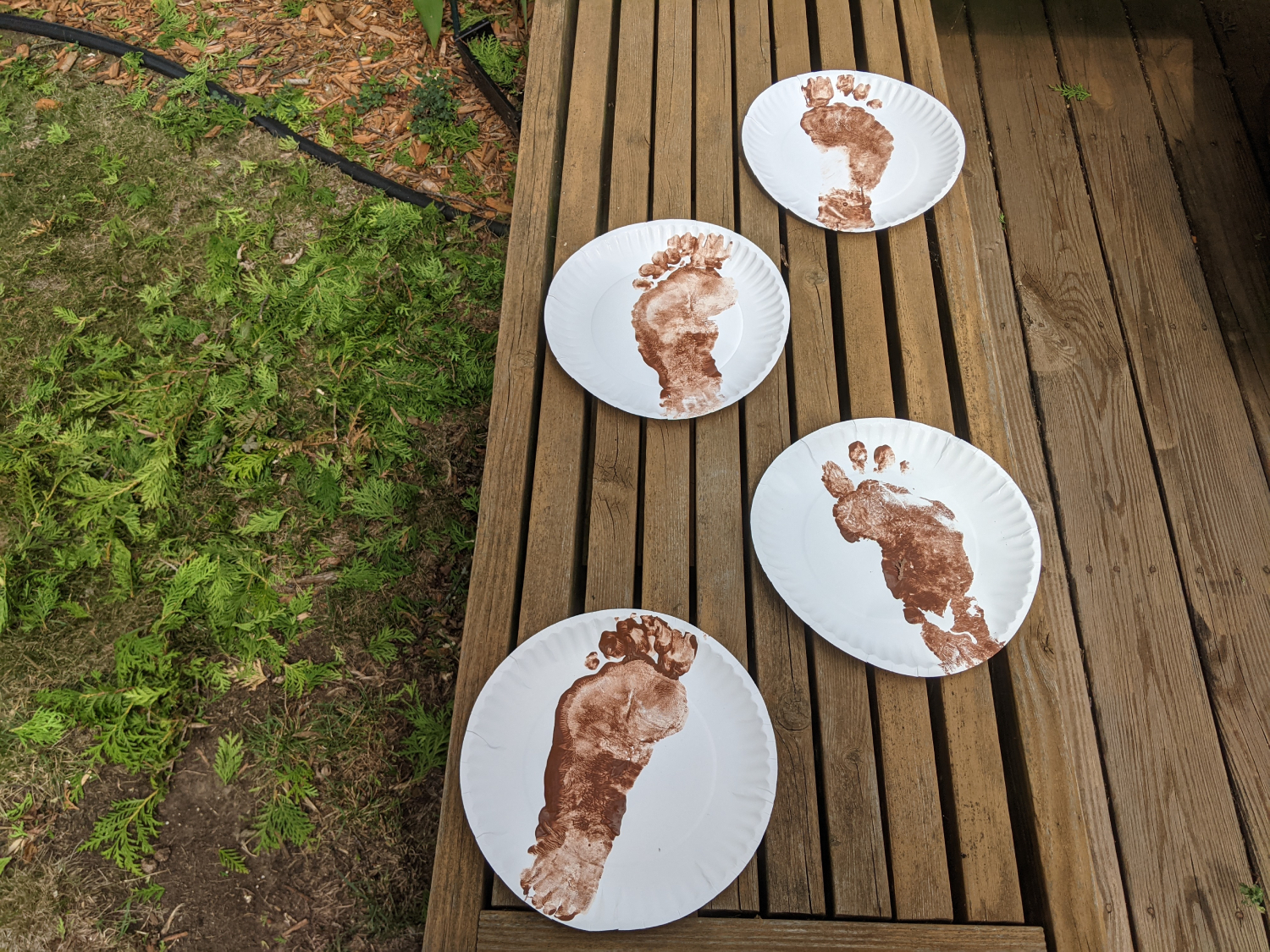 Paper plates with painted footprints are drying on a wooden porch