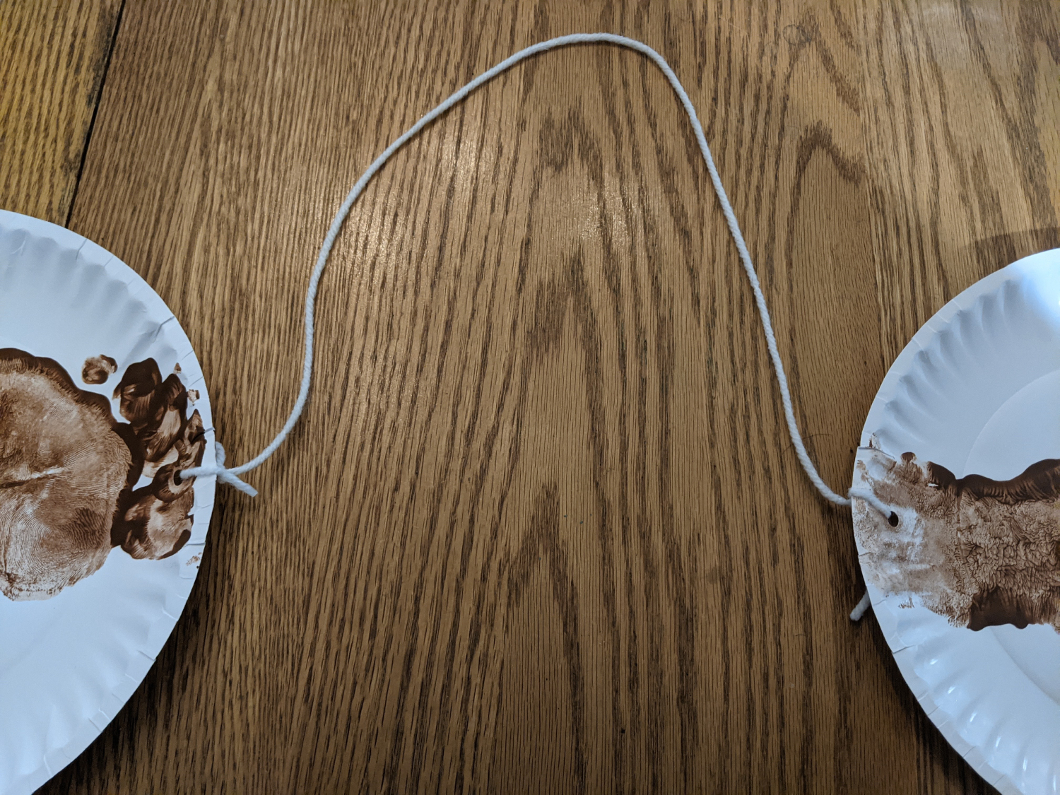 Two paper plates with painted footprints are tied together with a bit of string
