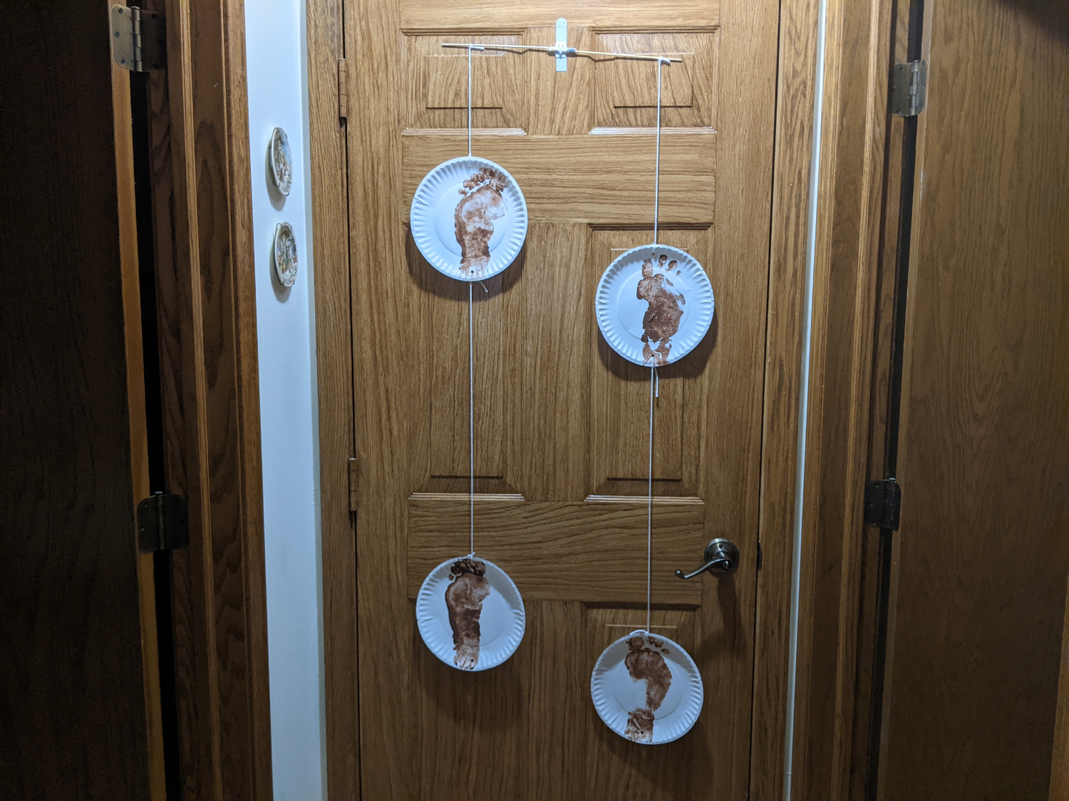Paper plates with painted footprints are hanging on the back of a door 