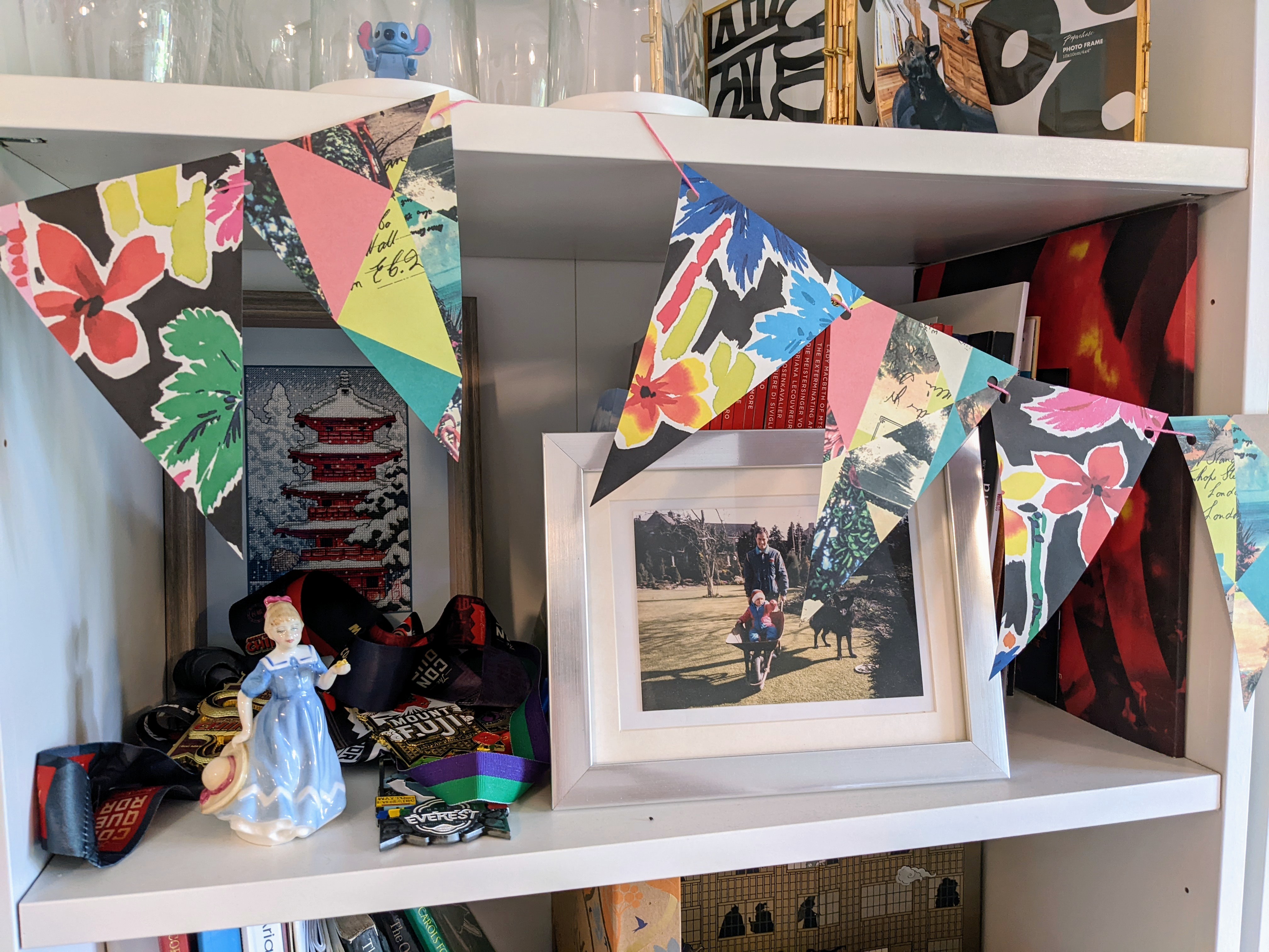 A close-up of some of the paper bunting in front of a shelf that has a framed photo and some small figurines. The bunting is a colorful floral pattern and looks very nice with the white bookshelves. 