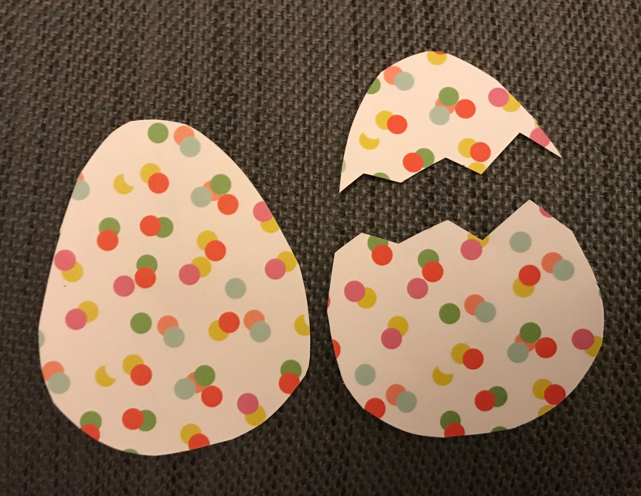 Two egg shapes cut out of colorful polka dot paper, with one egg cut into two "cracked" halves with a zig-zag line 