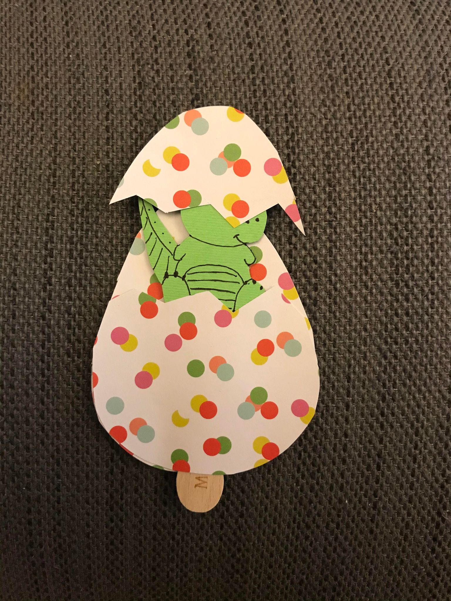 Close-up of the finished dinosaur craft; the top egg piece has caught over the little dino's eyes in an endearing sort of way.