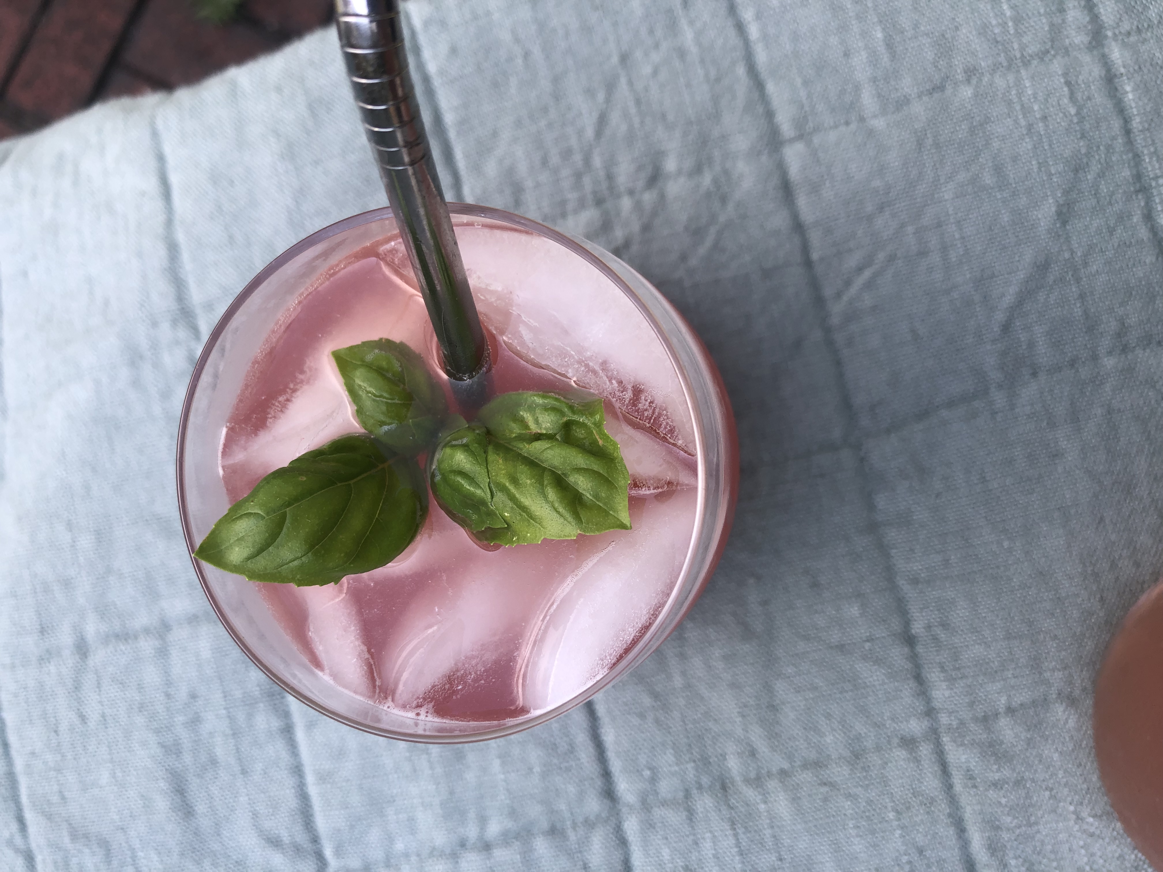 top view of a drink that is pink with a sprig of mint; a straw sticks out of one side of the glass