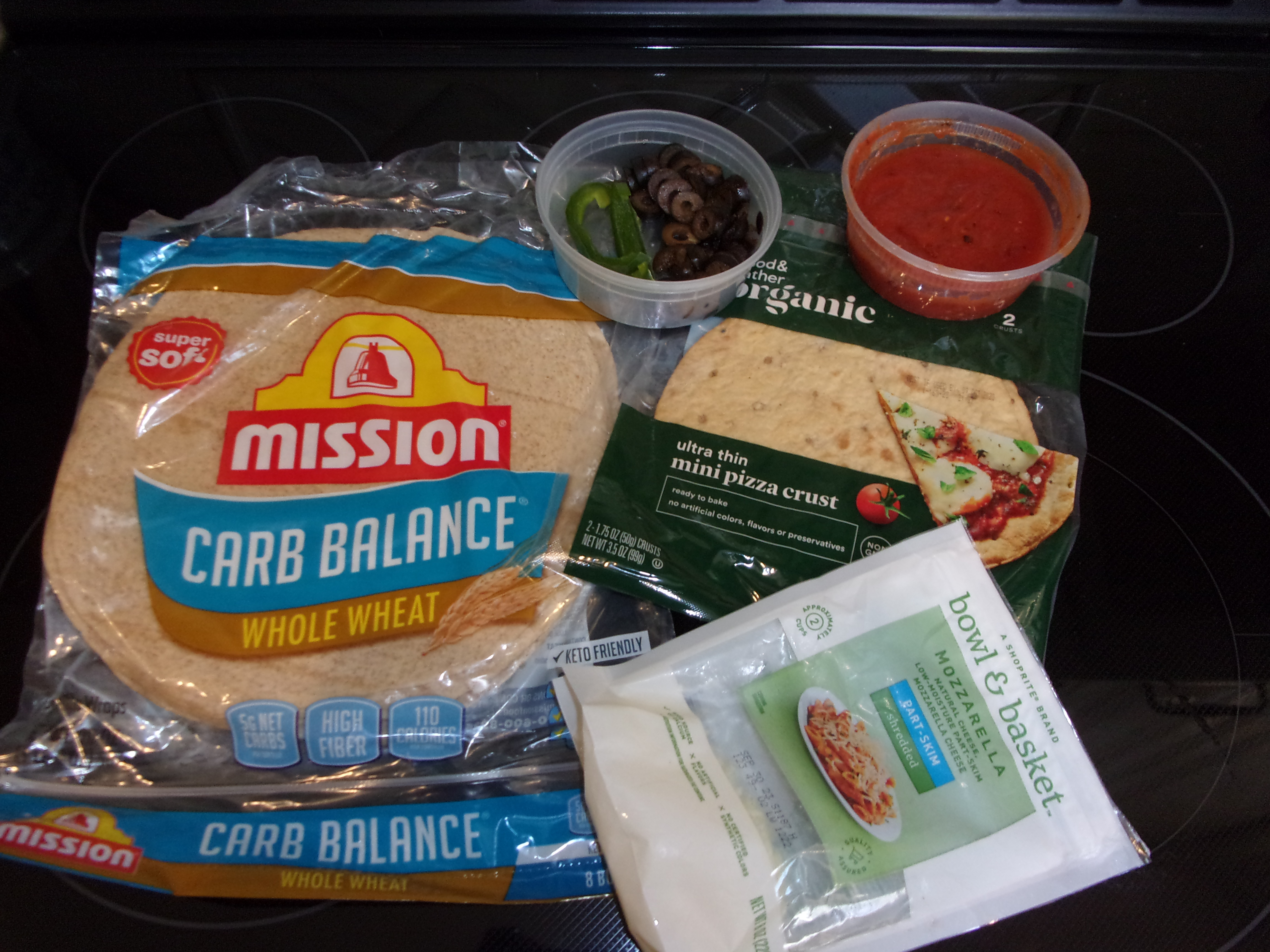 ingredients laid out on a counter including tortillas, cheese, pizza sauce, and assorted peppers 
