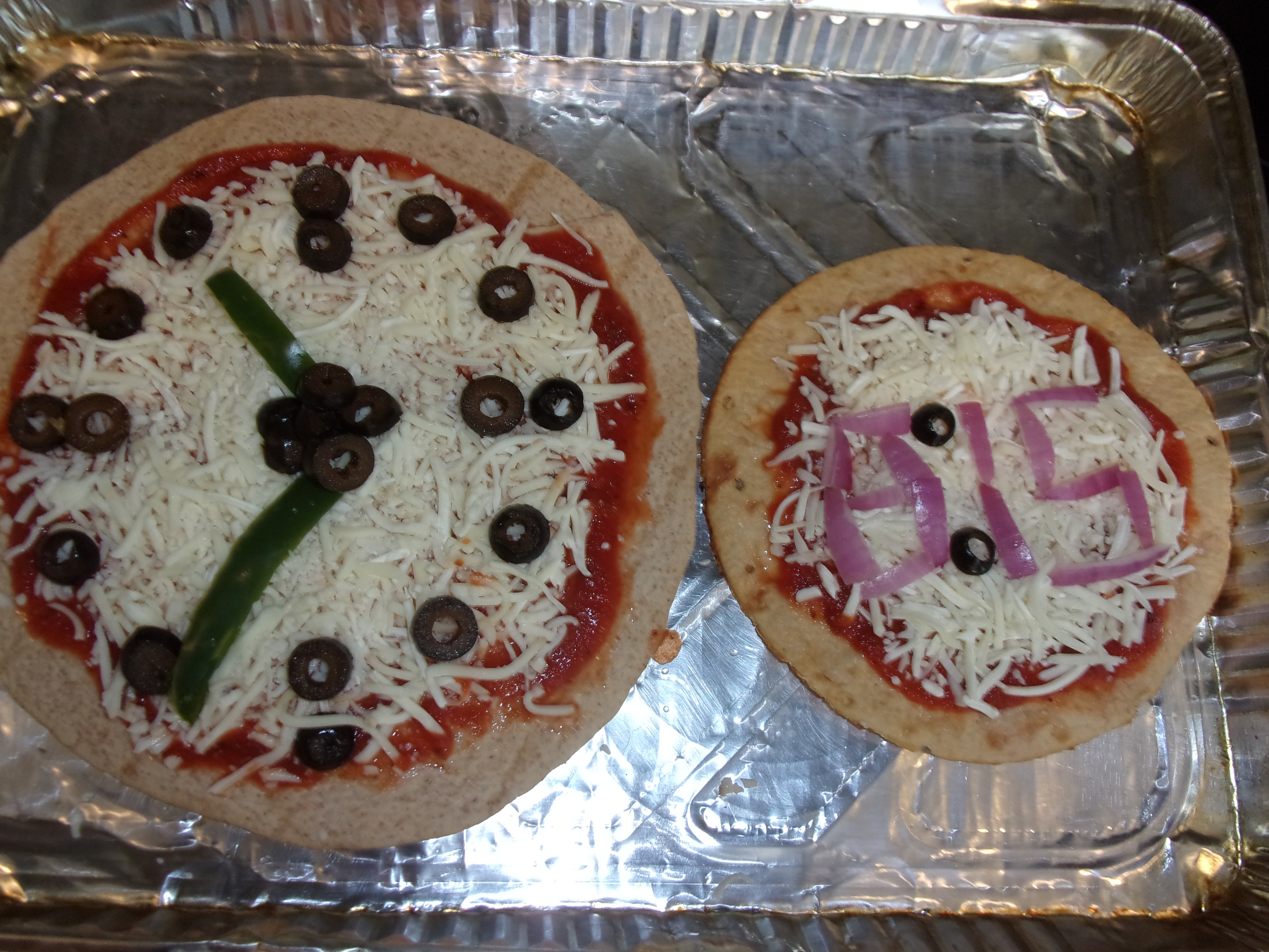 two pizzas with toppings placed to look like clocks. one is analog, using peppers to make the time approximately 11:35; the other is "digital" using onions to write out "8:15"
