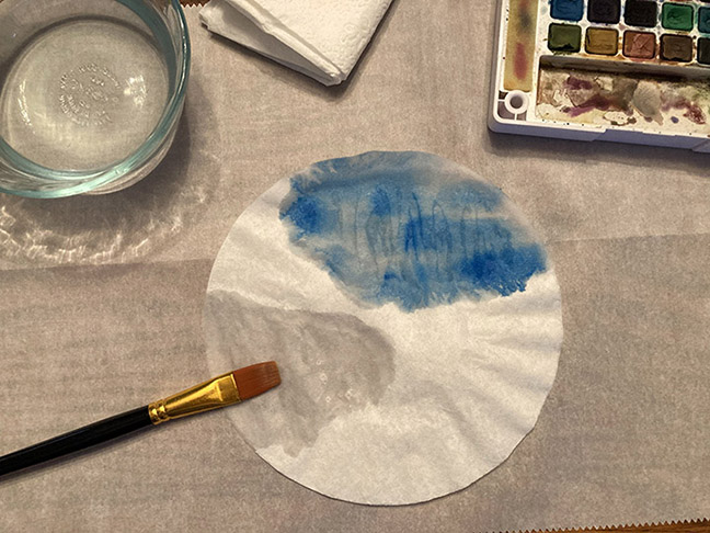 blue watercolor paint is applied to a coffee filter