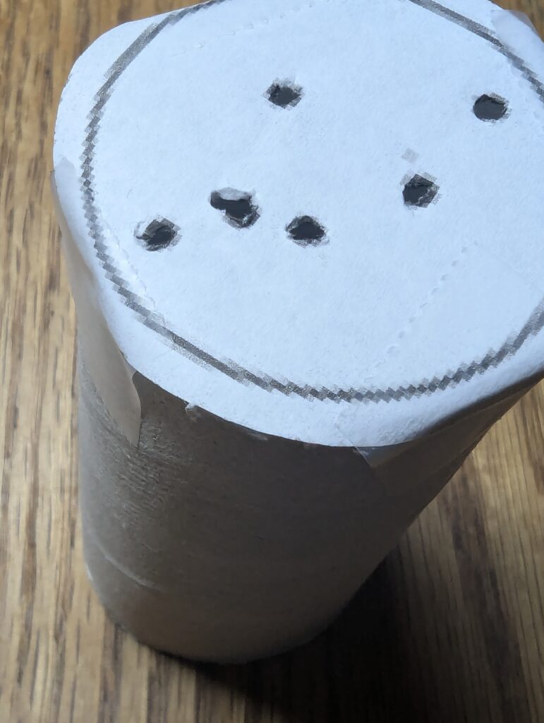 a stencil with holes punched into a constellation pattern is taped onto a toilet paper/loo roll tube