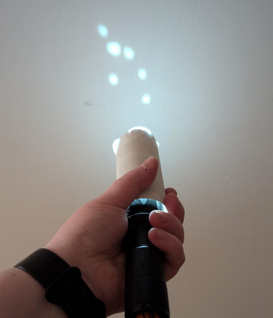 someone holds the paper tube with the flashlight inside so it points at a wall, projecting "stars" of light