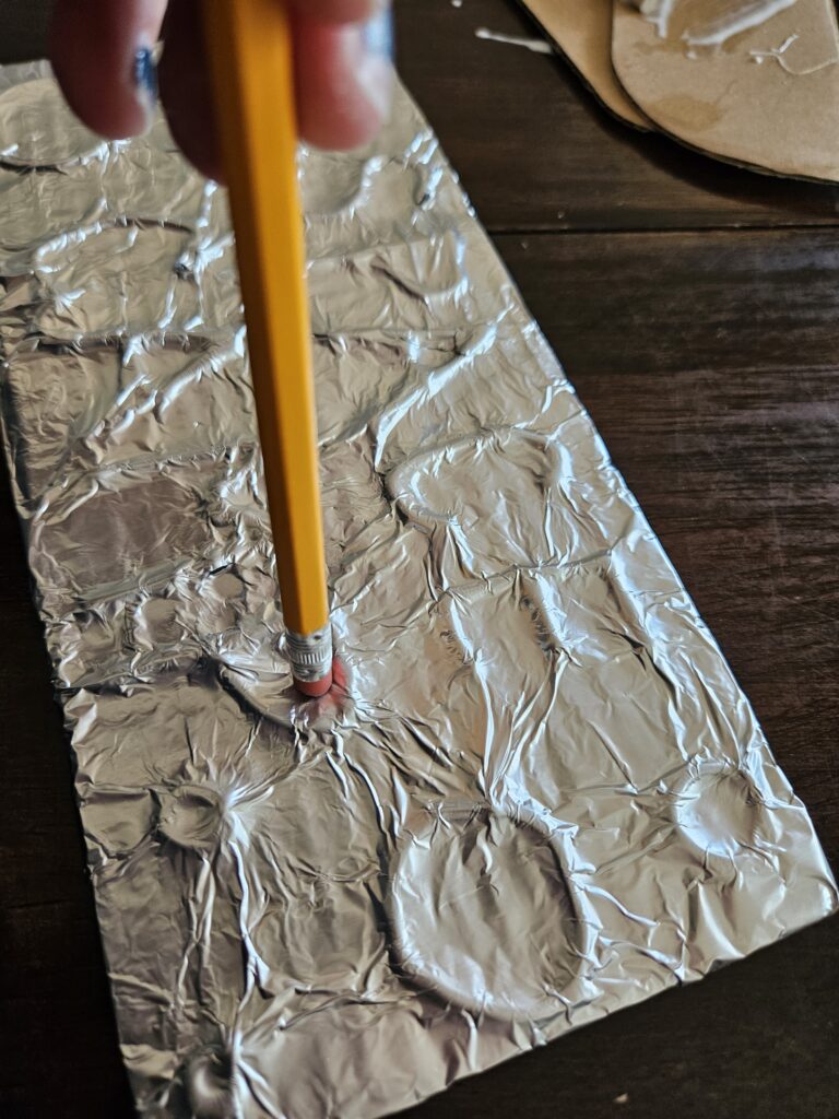 using a pencil eraser to press the foil onto the design