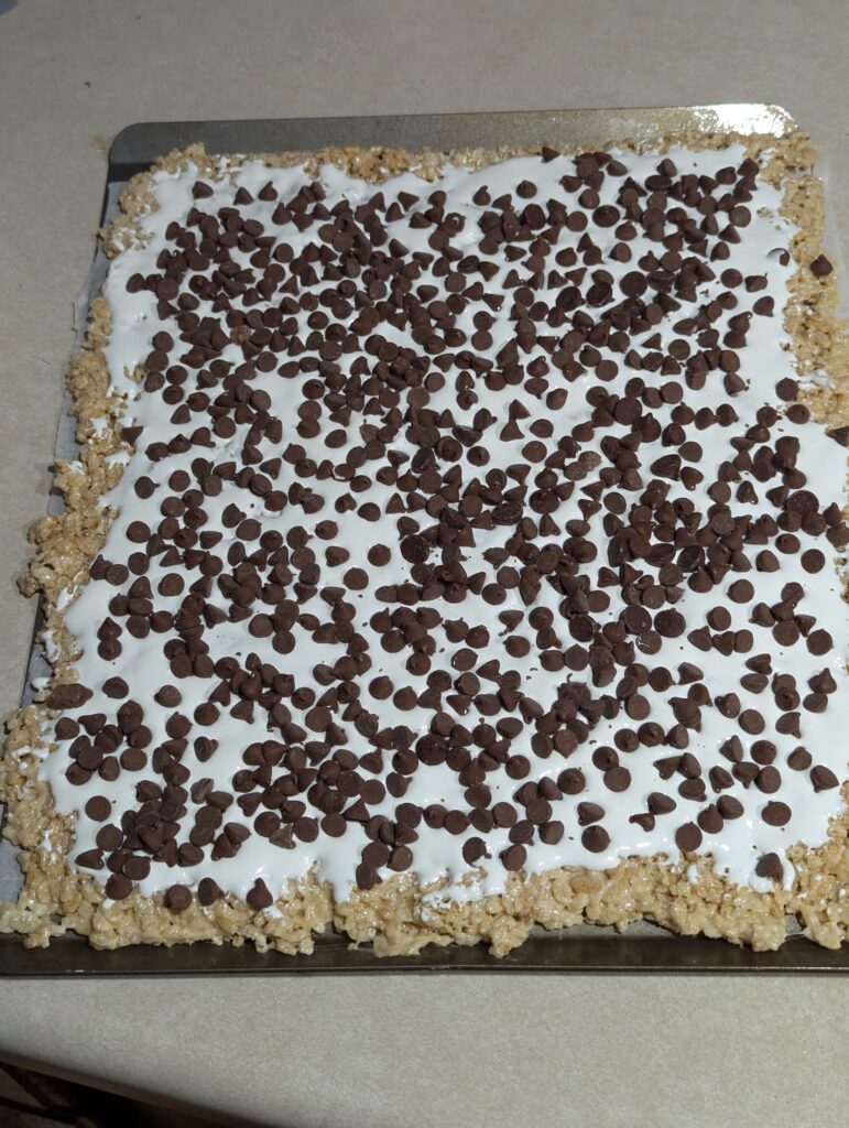 rice krispy rolled flat on a pan and then covered with marshmallow fluff and chocolate chips