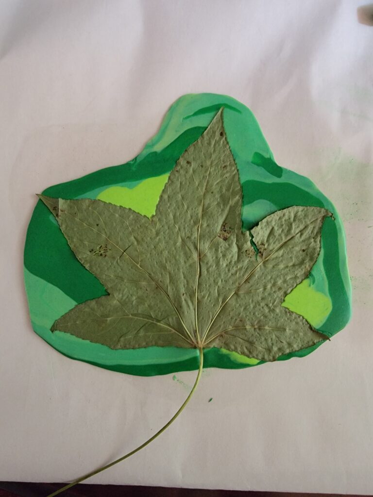 a large leaf is pressed onto the top of the flat clay