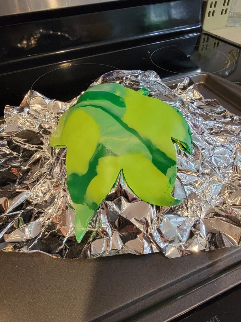 the leaf has been removed and the cut clay shape is resting in a curve shape (upside-down) on some balled up foil