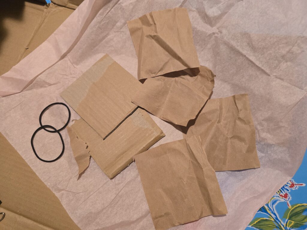 2 squares of cut cardboard and several squares of brown paper cut to the same size are arrayed across the surfact
