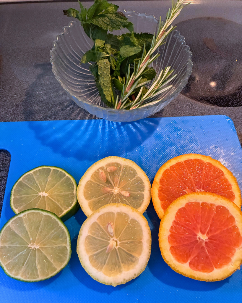 sliced citrus laid out on a blue cutting board and sprigs of fresh herbs in a clear glass to the side