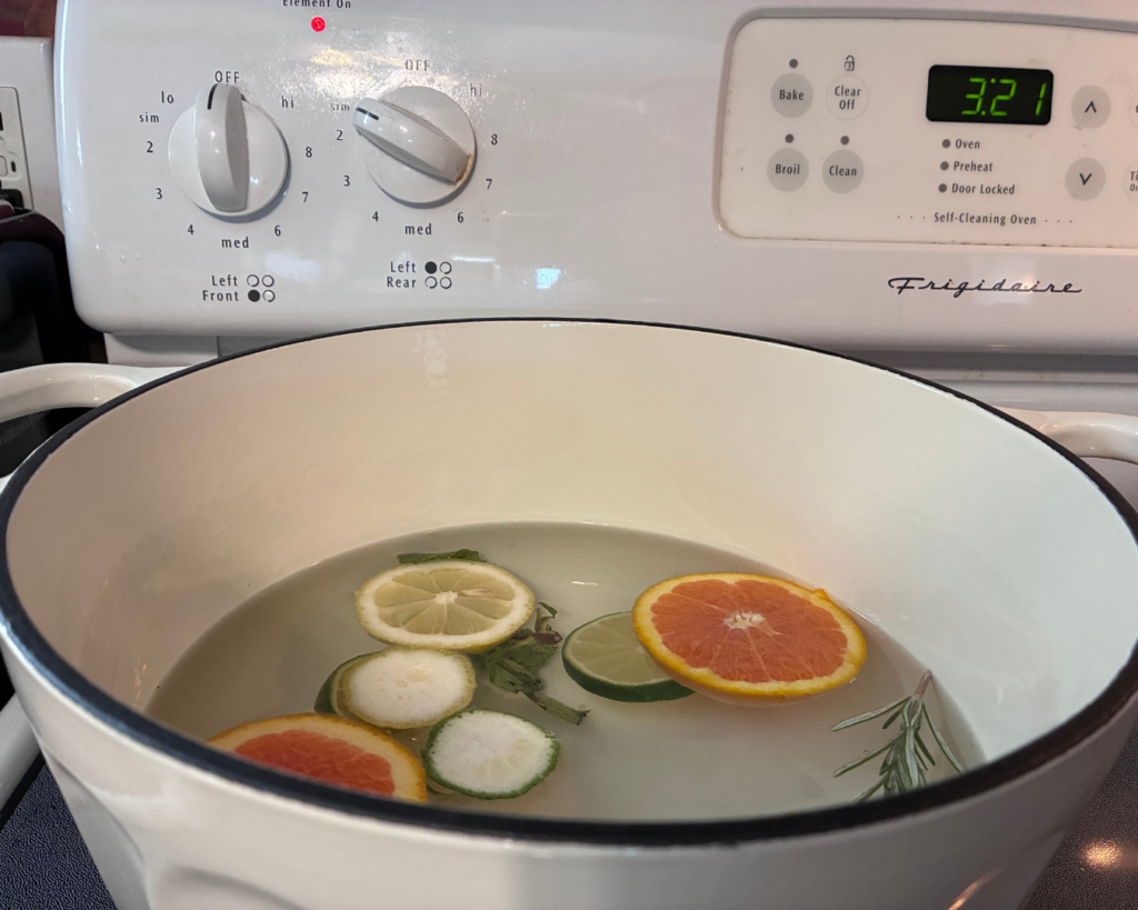 the white bowl is on the stovetop with the sliced citrus and fresh herbs floating in water