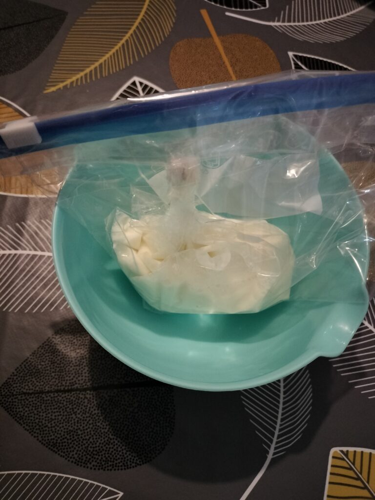 a ziploc bag with cream inside rests inside a blue bowl