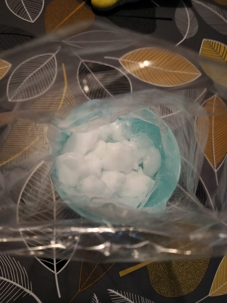 the bag with cream inside has been placed inside another bag with ice (so, big bag has ice and small bag); all are resting in the blue bowl