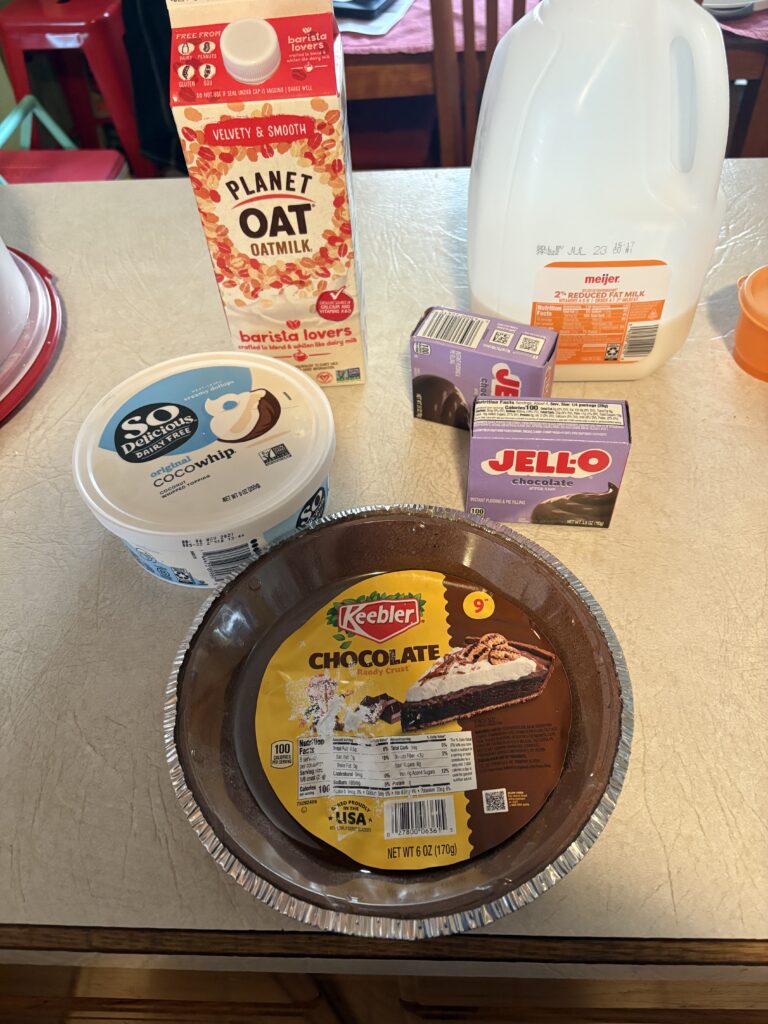 Supplies for no-bake pudding pie including pie crust, pudding mix, whipped topping, milk