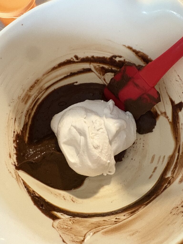 a mixing bowl with a red spoon, folding together whipped topping and chocolate