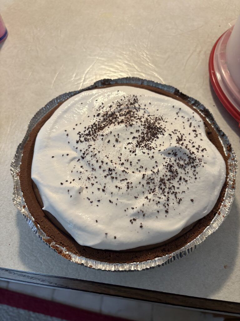 completed no-bake pudding pie is in a chocolate crust with whipped topping and chocolate shavings on top
